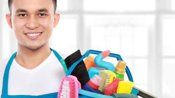 Smiling professional cleaner holding a bucket filled with colourful cleaning supplies for spring cleaning and home care.