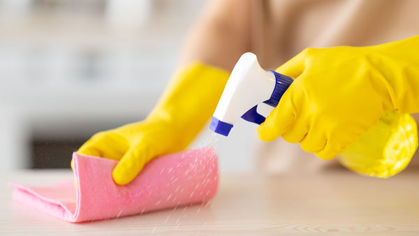Close-up of cleaner wearing yellow gloves spraying solution on a cloth for detailed move-in and move-out cleaning.
