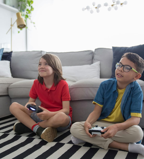 Two kids sitting on a striped rug in a living room playing video games on the floor near the couch.