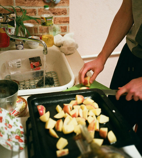 Person chopping apples on a cutting board beside a kitchen sink with dishes and running water, showing a busy food prep area.