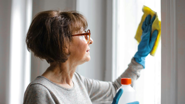 Woman wearing gloves cleaning a window with a cloth and natural solution, promoting a fresh and chemical-free home environment.
